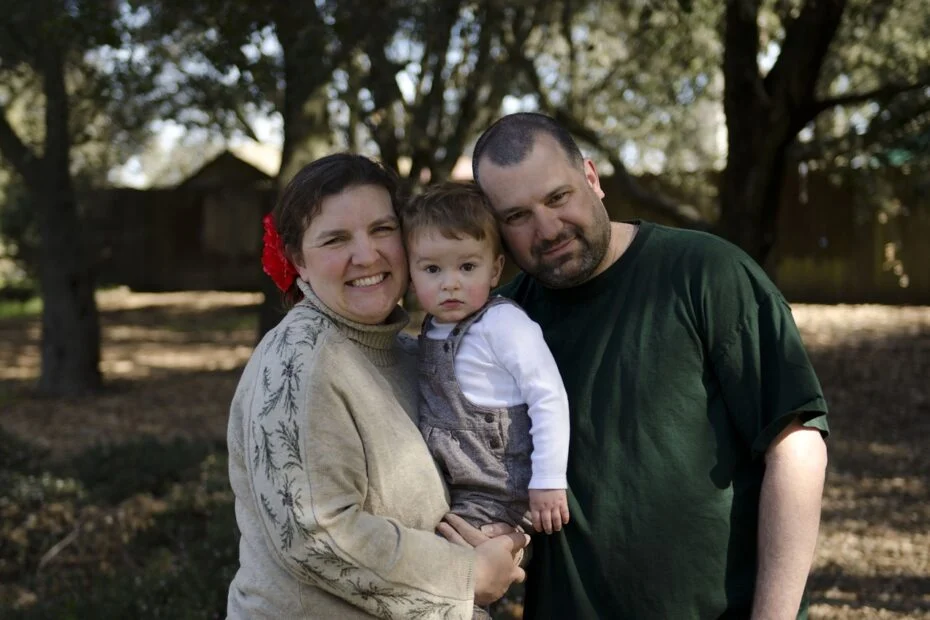 Madre y padre sonrientes posan al aire libre con su hijo pequeño en brazos, en alusión al cuidado familiar