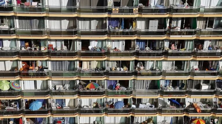 Fachada de un bloque de apartamentos con decenas de balcones llenos de sombrillas, sillas y enseres de verano