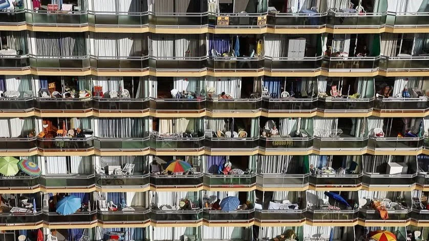Fachada de un bloque de apartamentos con decenas de balcones llenos de sombrillas, sillas y enseres de verano