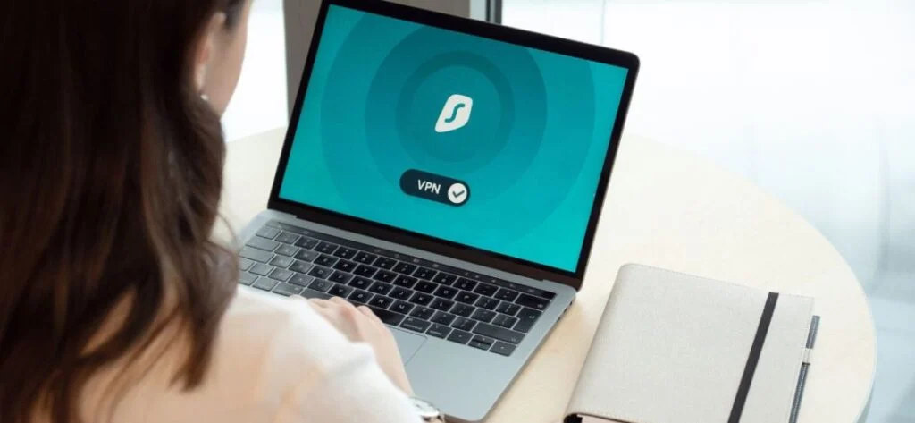 Mujer usando un portátil con la conexión VPN activada en pantalla junto a una libreta, en alusión a la ciberseguridad