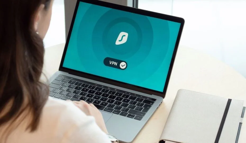 Mujer usando un portátil con la conexión VPN activada en pantalla junto a una libreta, en alusión a la ciberseguridad