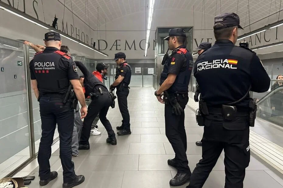 Agentes de los Mossos d'Esquadra y de la Policía Nacional cachean a varias personas junto a la pared acristalada de un pasillo